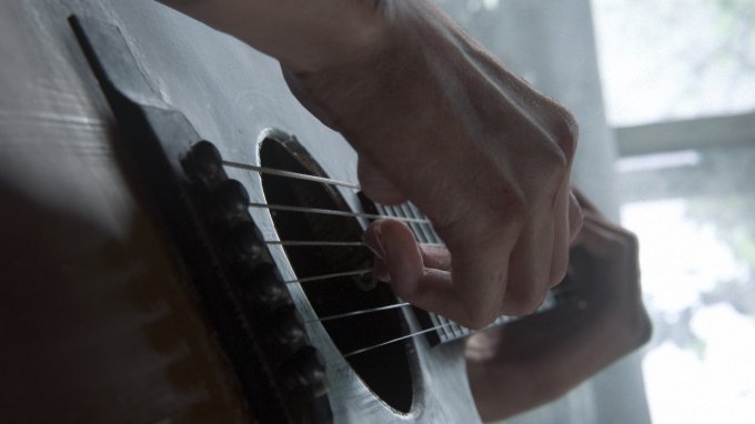 Mãos de Ellie tocando violão.