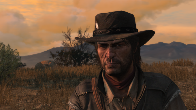 Close no rosto do personagem John Marston, ao ar livre no final do dia. Ele usa um chapé de cowboy, tem uma cicatriz no rosto e barba por fazer. Ao fundo uma vegetação rasteira e seca compõe o cenário.