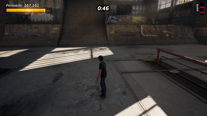 Cena do jogo em um skatista andando dentre de um grande armazém que abriga uma pista de skate, com divesos graffitis espalhados.